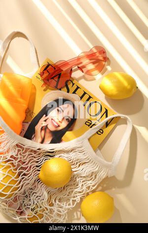 Schnur-Tasche mit frischen Zitronen, Modemagazin und Strandaccessoires auf beigefarbenem Hintergrund, flacher Lay Stockfoto