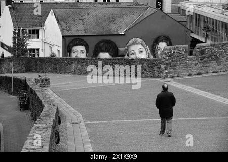 Man läuft auf den Stadtmauern von Derry/Londonderry, Nordirland, mit einem Wandbild der englisch/irischen TV-Serie Mural Derry Girls im Vordergrund. Stockfoto