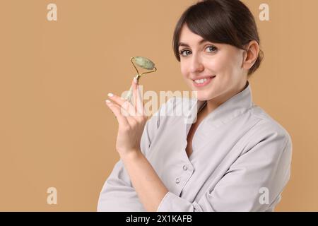 Kosmetologe mit Gesichtsrolle auf beigefarbenem Hintergrund Stockfoto