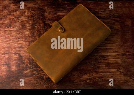 Umschlagmappe aus echtem Leder für Notizblock der Größe A5 auf dunklem Holzhintergrund. Stockfoto
