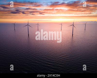 Sonnenuntergang beleuchtet Windturbinen im Ozean und schafft eine atemberaubende natürliche Landschaft Stockfoto
