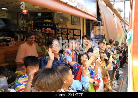 Maeklong, Thailand - Touristen, die mit ihren Smartphones den Zug nehmen, der durch den Bahnmarkt in der Nähe der Verkaufsstände fährt Stockfoto