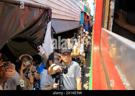 Maeklong, Thailand - aus dem Kutschwagen sehen, wie die Menschen Smartphones benutzen, um Züge zu erfassen, die durch den Bahnmarkt in unmittelbarer Nähe der Verkaufsstände fahren Stockfoto