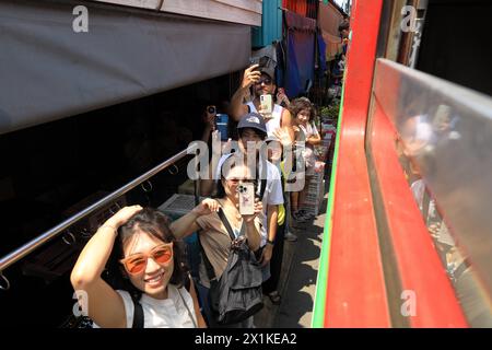 Maeklong, Thailand - aus dem Kutschwagen sehen, wie die Menschen Smartphones benutzen, um Züge zu erfassen, die durch den Bahnmarkt in unmittelbarer Nähe der Verkaufsstände fahren Stockfoto