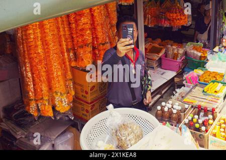 Maeklong, Thailand - Ein Stallhalter benutzt sein Smartphone, um den Zug zu erfassen, der ganz in der Nähe der Stände durch den Bahnmarkt fährt Stockfoto