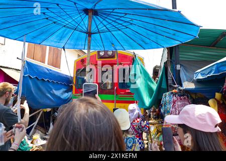 Maeklong, Thailand - Touristen, die mit ihren Smartphones den Zug nehmen, der durch den Bahnmarkt in der Nähe der Verkaufsstände fährt Stockfoto