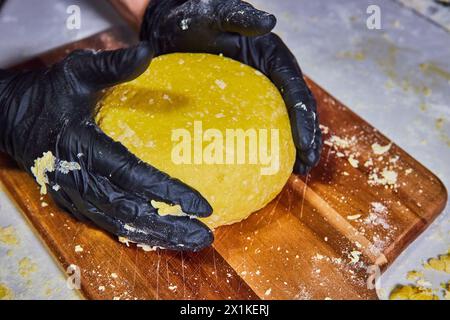 Handwerklicher Teig kneten mit Handschuhen auf Holzbrett Stockfoto