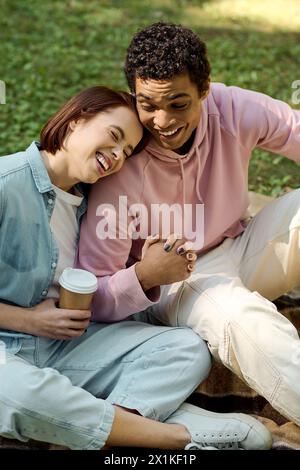 Ein vielseitiges Paar in lebendiger Kleidung sitzt friedlich auf dem Boden und genießt die Gesellschaft der anderen in einer Parklandschaft. Stockfoto