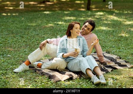 Ein vielseitiges Paar in lebendiger Kleidung sitzt auf einer Decke im Gras und genießt einen friedlichen Moment im Park. Stockfoto