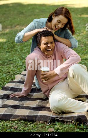 Ein vielseitiges, liebevolles Paar, das auf einer bunten Decke im Park sitzt und intime Momente miteinander teilt. Stockfoto