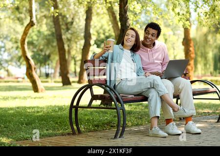 Ein vielseitiges Paar, das auf einer Parkbank sitzt und an einem Laptop arbeitet, umgeben von der Natur. Stockfoto