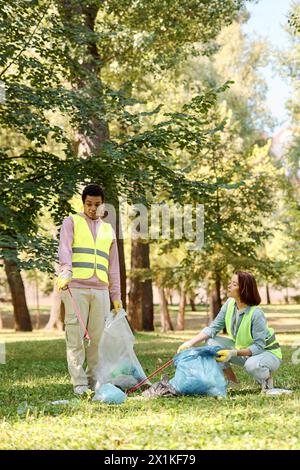 Ein vielseitiges Paar in Sicherheitswesten und Handschuhen steht im Gras und reinigt gemeinsam einen Park. Stockfoto