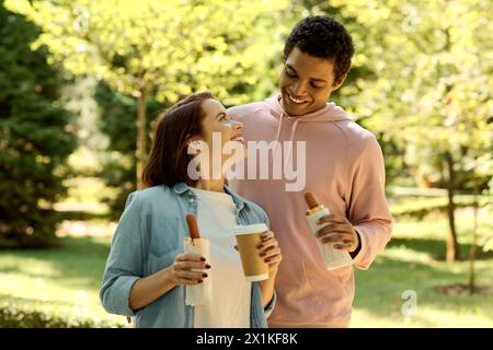 Ein stilvolles und vielseitiges Paar, das sich in Begleitung der anderen genießt, während es Kaffeetassen in einem lebhaften Park hält. Stockfoto