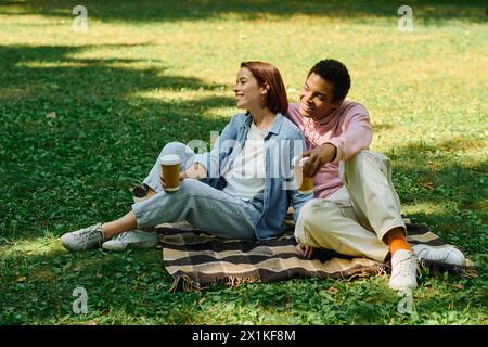 Ein vielseitiges Paar in lebendigen Gewändern, das auf einer Decke im Gras sitzt und sich gegenseitig in Gesellschaft freut. Stockfoto
