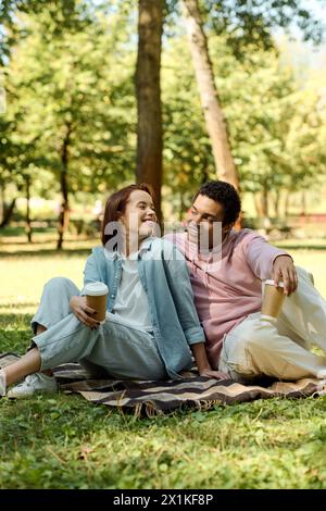 Ein vielseitiges Paar sitzt auf einer Decke im Park und genießt sich in lebendiger Kleidung in Gesellschaft. Stockfoto