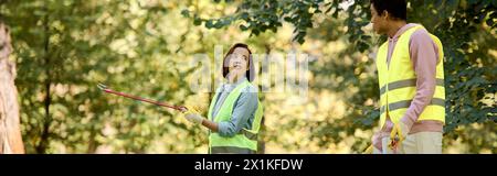 Ein vielseitiges, liebevolles Paar, in Sicherheitswesten und Handschuhen gekleidet, steht im ruhigen Wald. Stockfoto