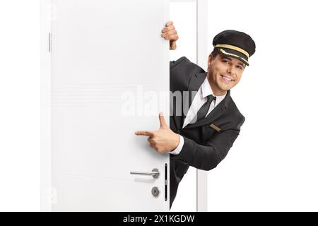 Lächelnder Mann in Uniform und Hut, der hinter einer Tür steht und isoliert auf weißem Hintergrund zeigt Stockfoto