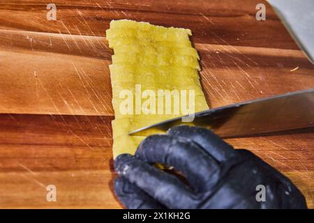 Koch schneidet gefaltete Pasta-Blätter auf gebrauchten Schneidebrettern, Ansicht auf Augenhöhe Stockfoto