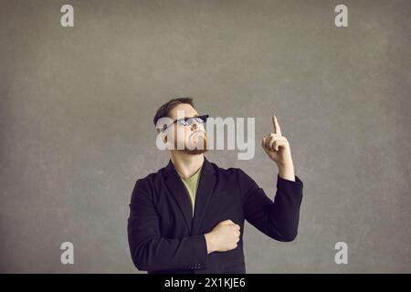 Lustiger Mann in einer Gangsterbrille denkt an eine kluge Idee und zeigt mit dem Finger nach oben Stockfoto