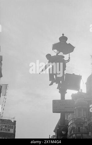 VE Day Scenes – rechts im Bild steht ein Mann auf einem Schild, der von einem Lampenpfosten aus in der Coventry Street ragt. Unter dem Mann befindet sich ein Schild, das die Fahrer zum Nuffield-Zentrum für H.M. Forces führt. Der untere Teil der Säule ist die Stütze für Ampeln. Im linken Hintergrund ist ein Horten für die Hollywoodkantine teilweise sichtbar. Von einem Baum bis hinter die Kamera. Das Foto wurde von Walter Lassally aufgenommen, einem jungen Mann, der sechs Jahre zuvor als Flüchtling in Großbritannien angekommen war. Jahre später erklärte Walter, dass er als Kind in Berlin von einer Parade erzählt wurde Stockfoto