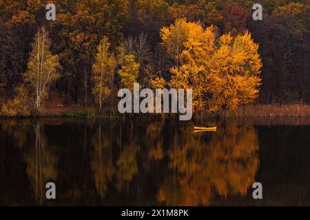 Mann im gelben Boot auf dem Fluss im goldenen Herbst, schöne Natur mit bunten gelben Bäumen und Reflexionen auf dem Wasser. Friedliche Natur, Ukraine. Stockfoto