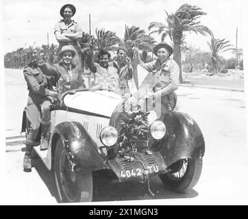 TUNIS - SZENEN NACH DEM FALL DER STADT - alliierte Soldaten mit Zivilisten um ein Auto in den Vororten von Tunis. Beachten Sie die Blumen auf der Vorderseite des Heizkörpers, British Army Stockfoto