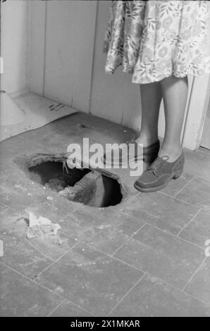 Ein TAG IM LEBEN Einer HAUSFRAU AUS KRIEGSZEITEN: ALLTAG IN LONDON, ENGLAND, 1941 - Mrs Day steht neben einem Loch im Boden, das durch eine Brandbombe gemacht wurde, bevor das Feuer unter Kontrolle gebracht wurde. Dieser Bereich des Hauses hat keine Asbestplatten auf dem Boden. Stockfoto