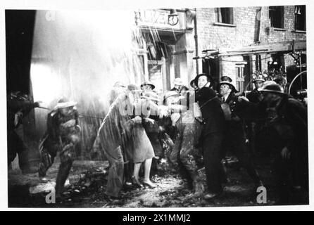 AFS FILM ACTORS: THE FILMING OF 'UNPUBLISHED STORY' IN DENHAM FILM STUDIOS, DENHAM, BUCKINGHAMSHIRE, ENGLAND, GROSSBRITANNIEN, 1941: als Teil des Films der Two Cities Film Company „Unpublished Story“, der in den Denham Studios gedreht wird, muss eine Mauer in der Nähe einer Telefonzelle einstürzen, in der einer der Schauspieler gerade einen Anruf getätigt hat. Dieses Foto zeigt Trümmer, wie sie sehr nahe an die Gruppe der Schauspieler und die Männer der Hilfsfeuerwehr und anderer ziviler Verteidigungsorganisationen im Film „agieren“, um den Film realistischer zu machen. Regie führte Harold French und die Hauptrollen Richard Greene und Valerie Hobson. Stockfoto