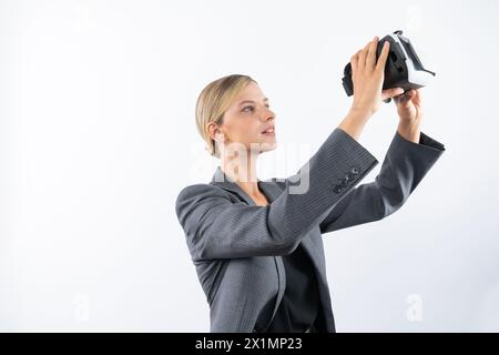 Kaukasische Geschäftsfrau hält VR-Glas, während sie auf weißem Hintergrund steht. Professioneller Projektmanager, der beim Tragen eine visuelle Reality-Brille sieht Stockfoto