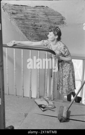 Ein TAG IM LEBEN Einer HAUSFRAU AUS KRIEGSZEITEN: ALLTAG IN LONDON, ENGLAND, 1941 - Mrs. Olive Day verbringt eine halbe Stunde oder so mit der Hausarbeit, bevor sie zur Arbeit geht. Hier sehen wir, wie sie die Bannister poliert. Über ihrem Kopf sehen wir ein großes Stück fehlenden Gips an der Decke, verursacht durch einen Luftangriff in der Nähe. Stockfoto