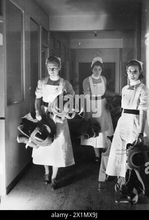 GASBOHRUNG IN Einem LONDONER KRANKENHAUS: GASMASKEN FÜR BABYS WERDEN GETESTET, ENGLAND, 1940 - Krankenschwestern tragen Babybeatmungsgeräte entlang eines Korridors als Teil einer Gasbohrung in einem Londoner Krankenhaus, 1940, Stockfoto