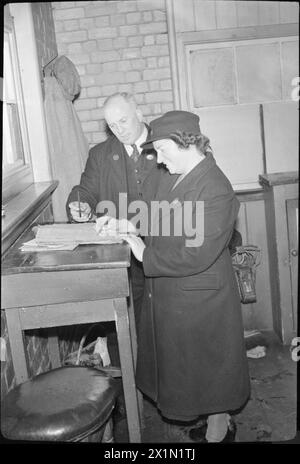 SERGEANT'S EHEFRAU AUS DEM NAHEN OSTEN MACHT SIGNALMAN'S JOB: LIFE AS A RAILWAY SIGNALWOMAN, MOLLAND, DEVON, ENGLAND, UK, 1943: Signalwoman Daisy Cook meldet sich am Molland-Stellwerk an, während Signalman Reg Westcott abschaltet. Das Hauptbuch, das sie unterzeichnen, wird als „Signalman's Bibel“ bezeichnet, und keine Schicht darf verlassen, bis die nächste Schicht unterzeichnet hat. Stockfoto