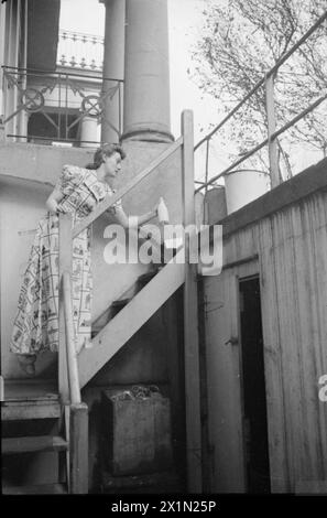 Ein TAG IM LEBEN Einer HAUSFRAU AUS KRIEGSZEITEN: ALLTAG IN LONDON, ENGLAND, 1941 - Mrs. Olive Day sammelt Milch und Zeitungen von der Treppe, die zum Keller ihres Hauses in South Kensington führt. Die Eimer, die auf der Straße oben auf der Treppe zu sehen sind, enthalten Sand und Wasser und werden im Falle von Feuerbomben bereitgestellt. Stockfoto