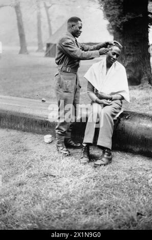 VICTORY MARCHERS CAMP IN LONDON: UNTERKUNFT IN KENSINGTON GARDENS, LONDON, ENGLAND, Großbritannien, 1946 - Ein Soldat der King's African Rifles übt seine Barbering-Fähigkeiten an einem Kollegen in seinem Lager in Kensington Gardens aus. Saidi rasiert den Kopf seines Freundes Ngette, während Ngette geduldig mit einem Handtuch um die Schultern sitzt. Stockfoto