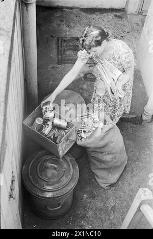 Ein TAG IM LEBEN Einer HAUSFRAU AUS KRIEGSZEITEN: ALLTAG IN LONDON, ENGLAND, 1941 - Mrs Day trennt Pappe und Blech von ihrem Hausmüll, bereit zur Bergung, außerhalb des Kellergeschosses ihres Hauses in South Kensington, London. Stockfoto