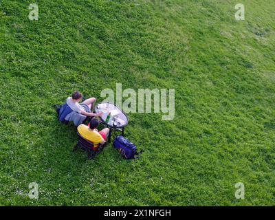 Aus der Vogelperspektive von oben auf zwei Einheimische, die sich ausruhen und entspannen, Picknick auf dem grünen Gras machen, während sie am Abend die natürliche Aussicht genießen, nein Stockfoto