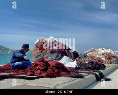 Nicht erkannte Fischer, die mehrere Werkzeuge von Fischernetzen oder Fangausrüstung und Seil, bunten Trawler, Waden und umliegenden Netzen am Seehafen vorbereiten Stockfoto