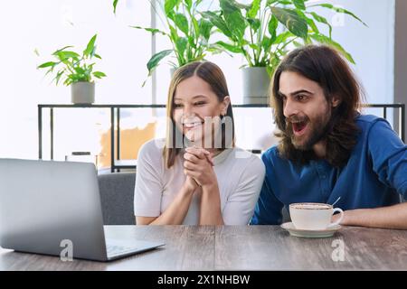 Glückliches überraschtes junges Paar, das zusammen in der Cafeteria auf den Laptop blickt Stockfoto