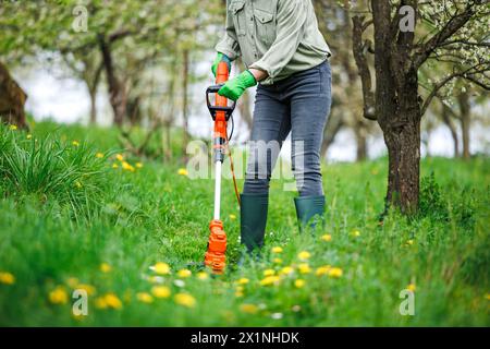 Gärtnerin trimmt Rasen mit einem Rasentrimmer. Frühjahrsgärtnerei Stockfoto