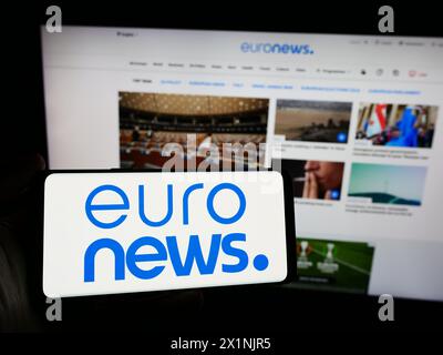 Person mit Smartphone und Logo des belgischen Nachrichtenunternehmens Euronews SA vor der Website. Schwerpunkt auf dem Display des Telefons. Stockfoto