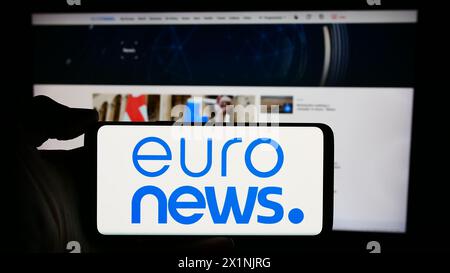 Person, die ein Mobiltelefon mit dem Logo des belgischen Nachrichtenunternehmens Euronews SA vor der Webseite hält. Schwerpunkt auf dem Display des Telefons. Stockfoto