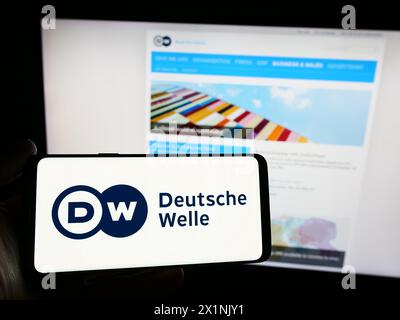 Person mit Smartphone und Logo der Deutschen Welle (DW) vor der Website. Schwerpunkt auf dem Display des Telefons. Stockfoto