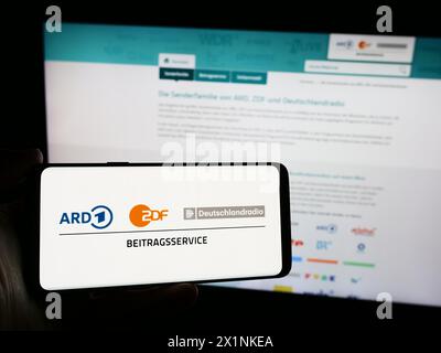 Person mit Smartphone mit Logo des ARD ZDF Deutschlandradio Beitragsservice vor der Website. Schwerpunkt auf dem Display des Telefons. Stockfoto