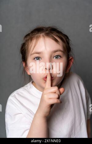 Ein kleines Teenager-Mädchen, das den Finger an den Mund hält und ein Zeichen von Stille zeigt. Hochwertige Fotos Stockfoto