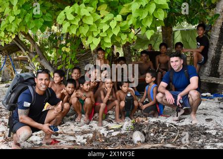 Woleai, Mikronesien, Föderierte Staaten Von. 12. April 2024. US-Küstenwache Lt. Ray Cerrato, Befehlshaber links, und Petty Officer 2. Klasse Eugene Halishlius, rechts, vom Wächter-Klasse Schnellreaktionsschneider USCGC Oliver Henry posieren mit einheimischen Kindern, nachdem sie mit Nothilfe angekommen sind. Techniker und ein Umkehrosmose-System zur Linderung des Trinkwassermangels durch Dürre auf der abgelegenen Insel, 12. April 2024 in Woleai, Bundesstaat Yap, Föderierte Staaten von Mikronesien. Quelle: CWO Sara Muir/USCG/Alamy Live News Stockfoto