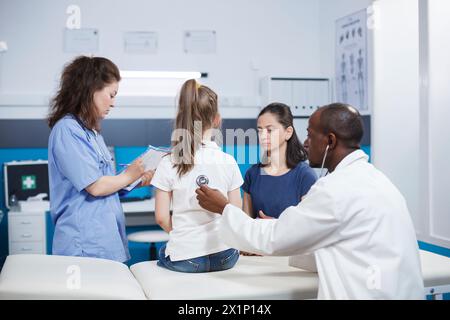 Bei der Untersuchung hört der Arzt den Herzschlag eines Kindes mit Stethoskop. Arzttermin im Gesundheitsamt untersucht der Hausarzt die Gesundheit eines jungen Mädchens mit Hilfe einer Krankenschwester. Stockfoto