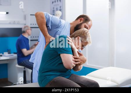 Kaukasische Seniorin wird von Physiotherapeutin untersucht. Der Patient, der sich von Rückenschmerzen erholt, wird einer Wirbelsäulendruckuntersuchung unterzogen und nimmt unter Anleitung rehabilitative Übungen an. Stockfoto