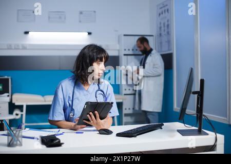 Die Krankenschwester verwendet ein intelligentes Tablet und einen Computer für medizinische Informationen und Untersuchungen. Bei der Untersuchung von Patientendaten auf einem Desktop-pc hält das medizinische Fachpersonal ein Gerät mit einem Touchscreen. Stockfoto