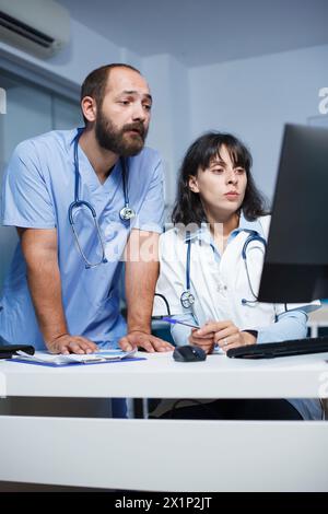 Medizinische Fachkräfte arbeiten in einem Krankenhaus zusammen, diskutieren über die Patientenversorgung und nutzen digitale Geräte wie Desktop-Computer. Effektive Kommunikation und Teamarbeit werden hervorgehoben. Stockfoto