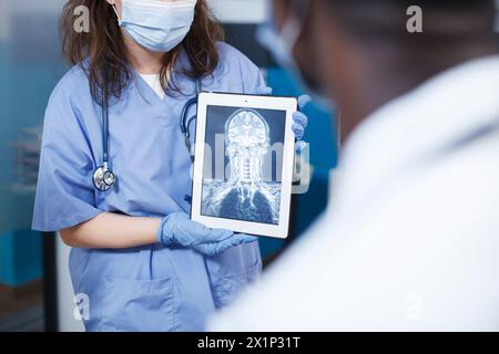 Arzt analysiert medizinische Ergebnisse für Patienten in einer Praxis. Untersuchung der Befunde mit einem digitalen Tablet und einem Bildschirm, auf dem ein Schädelscan angezeigt wird. Szene vermittelt Professionalität und Expertise in der Neurologie. Stockfoto